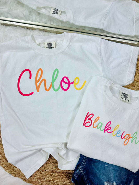 White t-shirts with colorful names 'Chloe' and 'Blakleigh' on a textured surface.