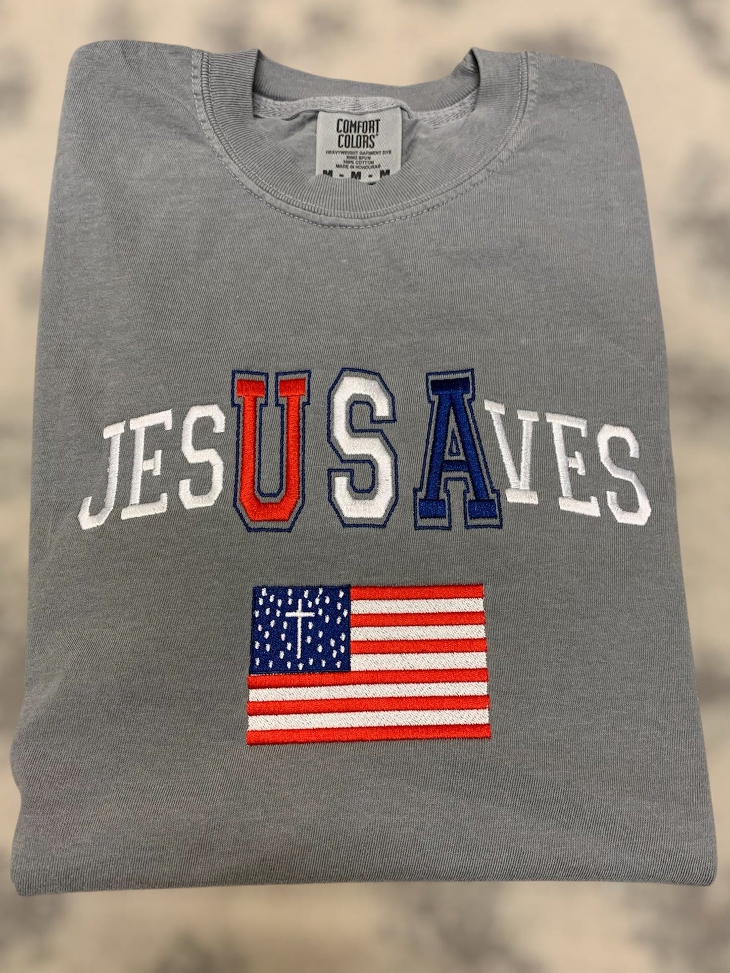 Gray t-shirt with 'JESUS SAVE' text and American flag on a beige background
